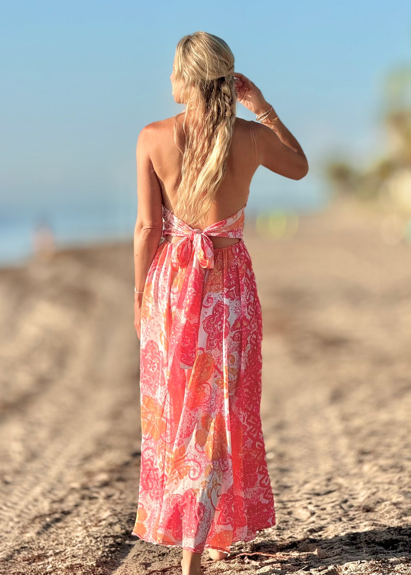 Woman in a pink floral dress standing on a sandy beach.