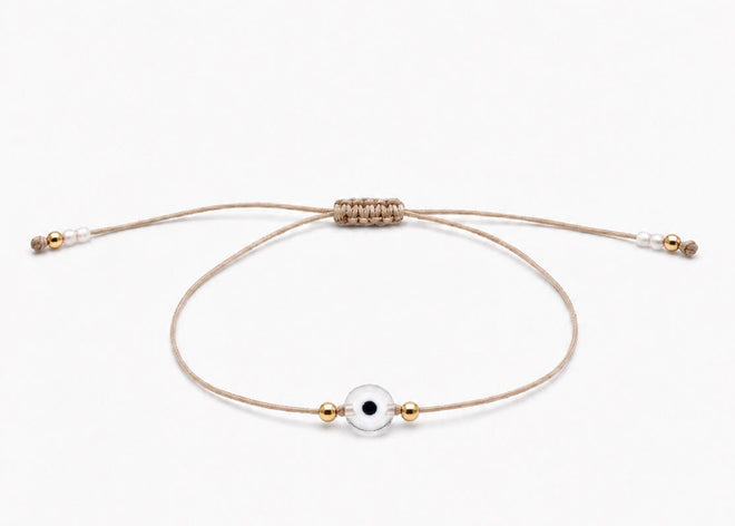 Delicate adjustable bracelet with a small evil eye charm and gold filled beads on a white background
