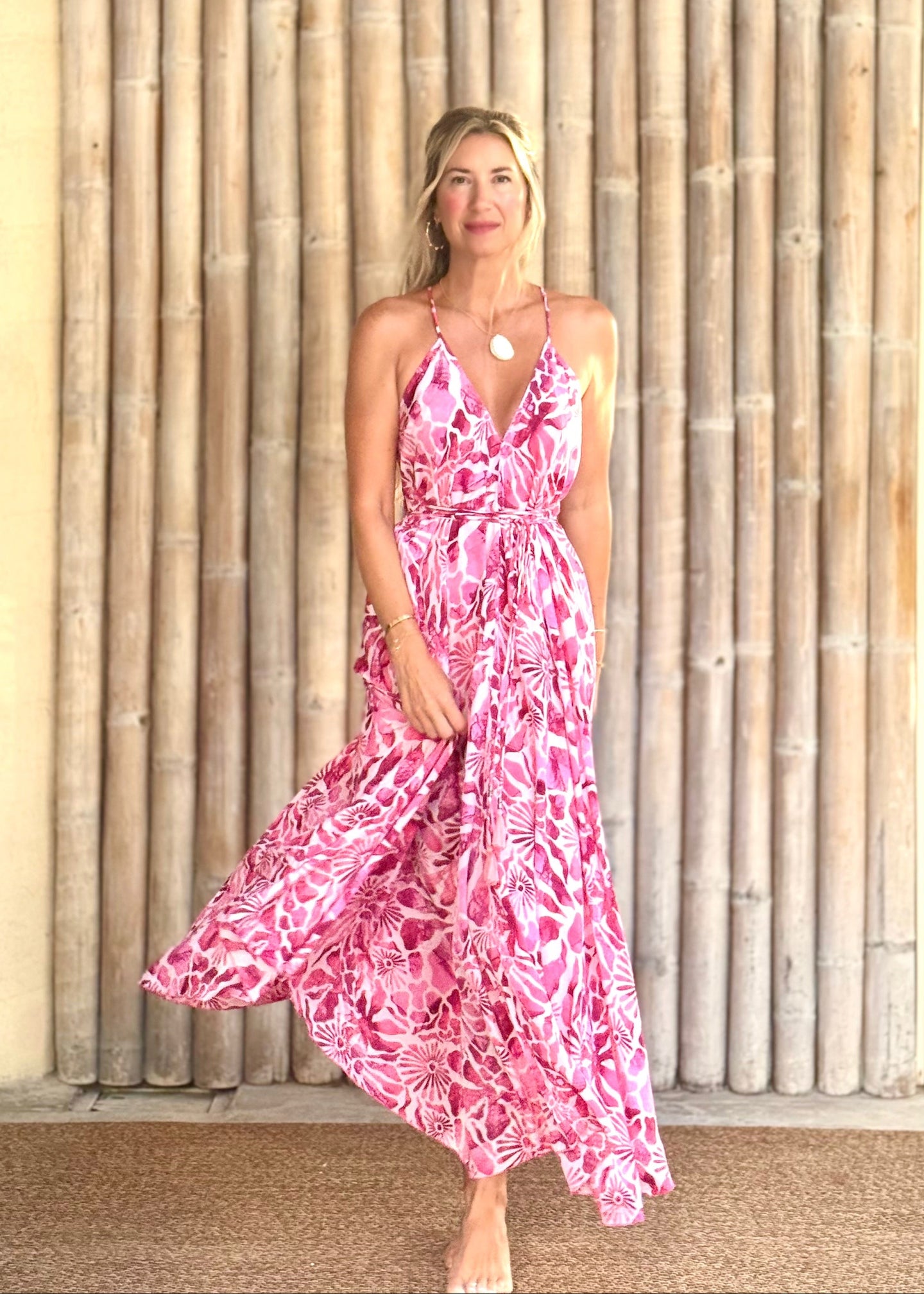 Woman in a pink floral dress standing outdoors with plants in the background