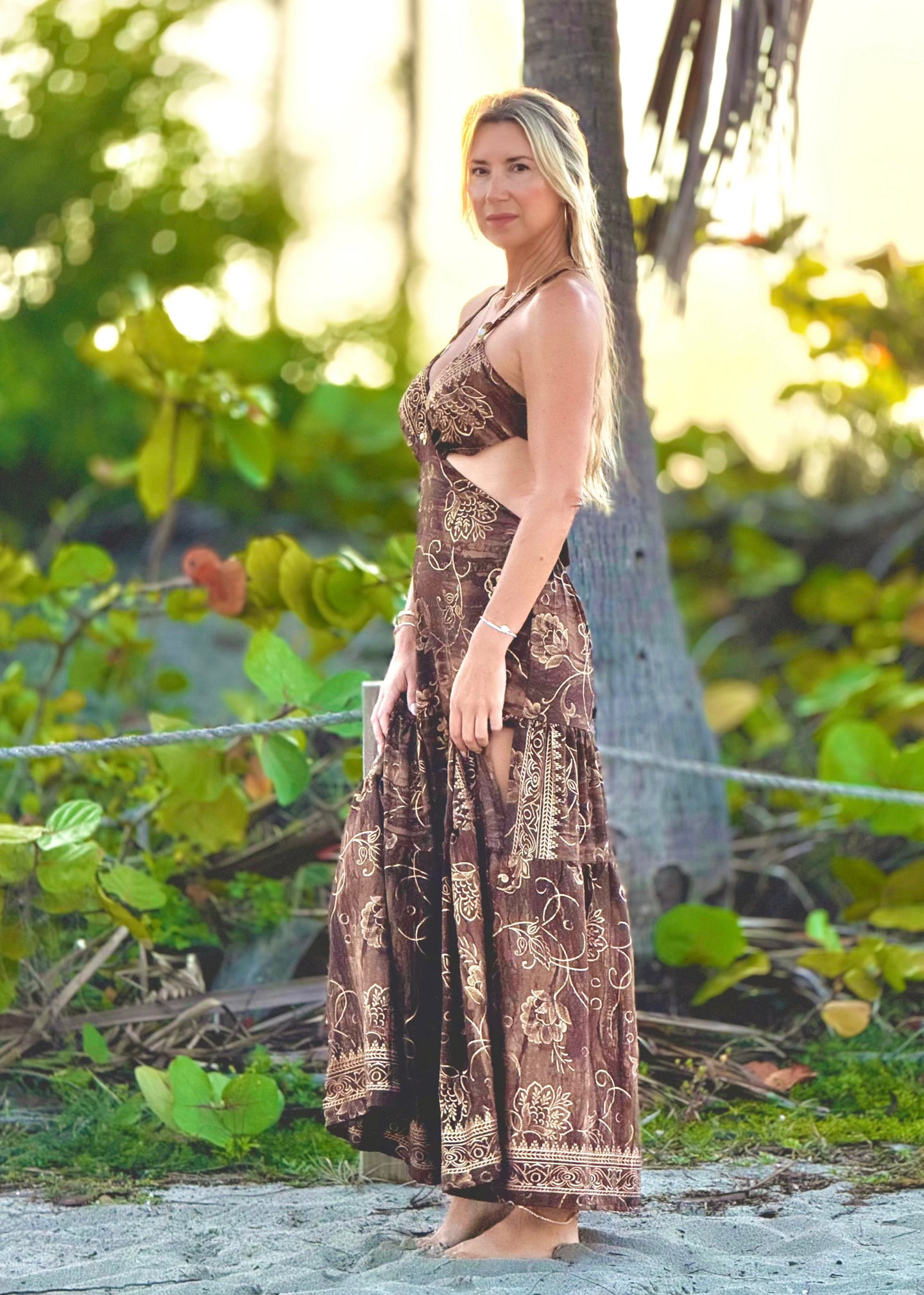 Woman in a patterned dress standing in a natural setting with trees and greenery.