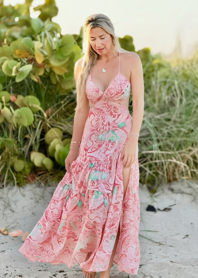 Woman in a pink floral dress standing on a beach with greenery in the background