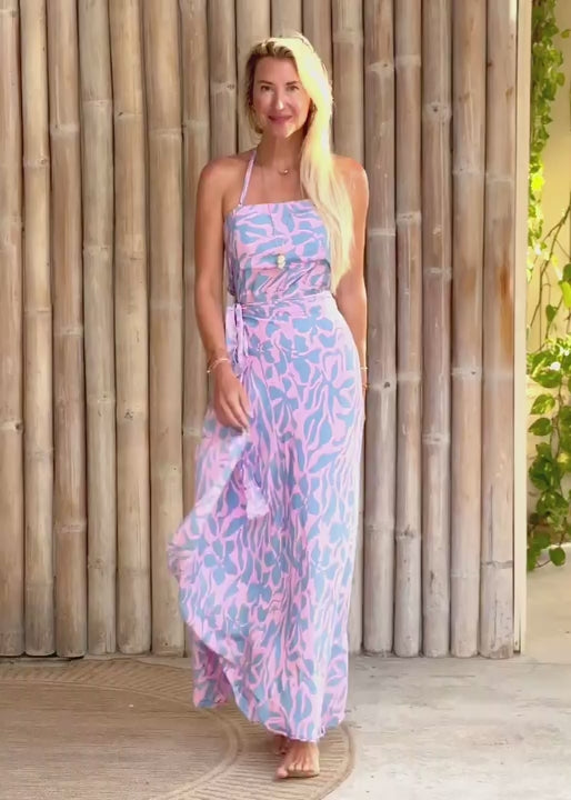 Woman wearing a blue and pink patterned dress standing against a wooden wall.