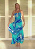 Woman wearing a blue and green patterned dress standing in front of a wooden shutter.