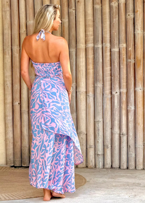 Woman wearing a pink and blue patterned dress standing against a wooden wall.