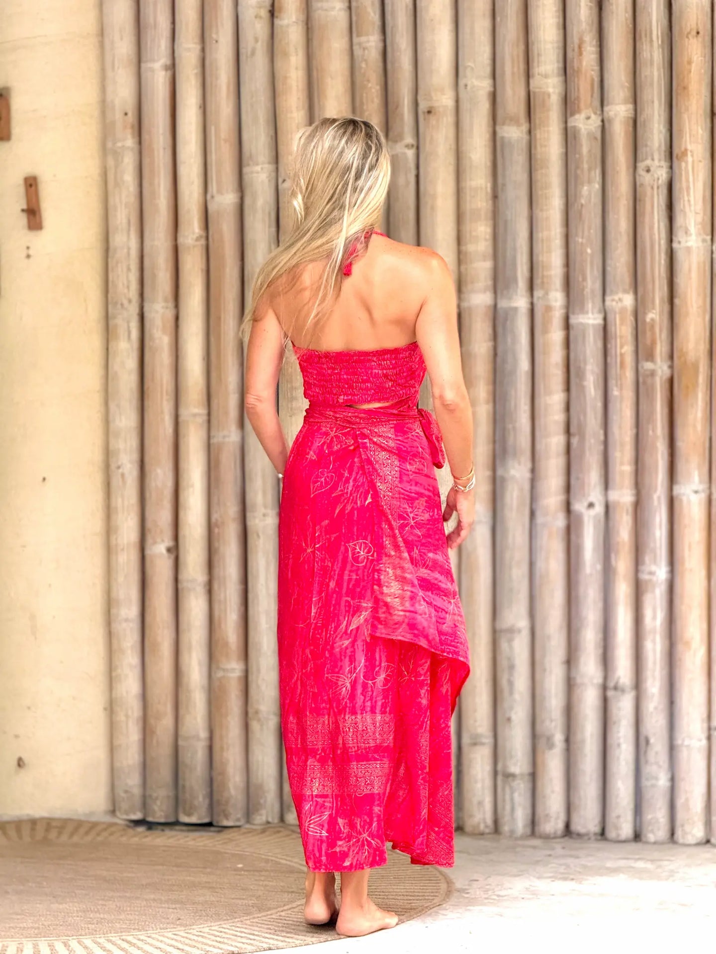 Woman wearing a bright pink dress standing against a wooden wall.