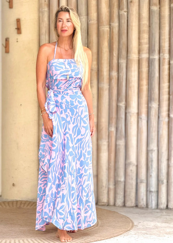 Woman wearing a blue and pink patterned dress standing against a wooden wall.